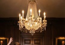 My mother-in-law slapped me so hard my head hit the oak wall, my sister-in-law spat on my military uniform, and my brother-in-law laughed while filming it like I was trash. They thought my husband was deployed thousands of miles away. I wiped the blood from my lip and said quietly, “You just made the biggest mistake of your lives.” Because five minutes later, the dining room doors exploded open—and everything changed.