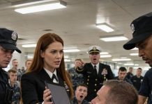 I noticed her before anyone else did—the quiet sailor in the corner, hiding behind auburn hair and a glowing tablet. Something about her didn’t fit. Then the mess hall doors slammed open, and a commander’s voice cut through the room: “Everyone stay exactly where you are.” My tray nearly slipped from my hands. The girl looked up, calm as stone. That was when I realized… she wasn’t just another sailor.