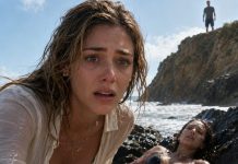 The police found my best friend wedged between the rocks beside the beach—her body covered in bruises, one leg twisted beneath her, her bikini torn. I dropped to my knees as her eyes suddenly opened. “He’s still here,” she whispered. “Who did this to you?” Her bloody fingers pointed toward a man watching from the cliffs. Then my phone vibrated with a photo of me sleeping—and one message: **You’re next.**